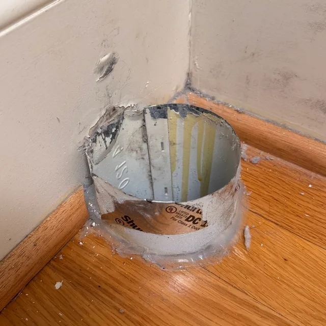Old dryer vent stub tight against a thick baseboard in Northern Shores Greensboro