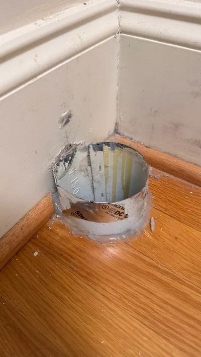 Old dryer vent stub tight against a thick baseboard in Northern Shores Greensboro