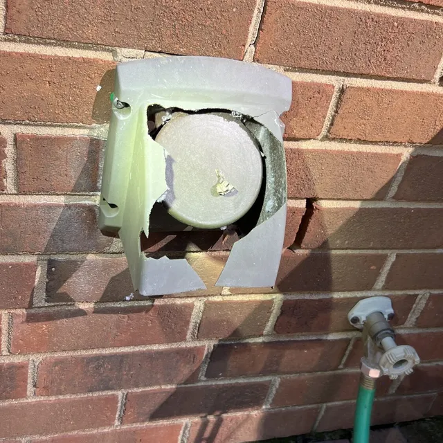 Cracked plastic dryer vent cover on a brick wall in Coble Farm Greensboro