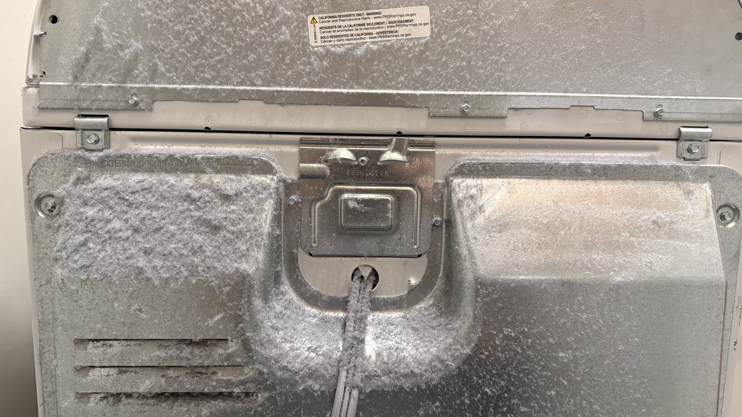 Lint and dust accumulated on the floor and wall behind a clothes dryer