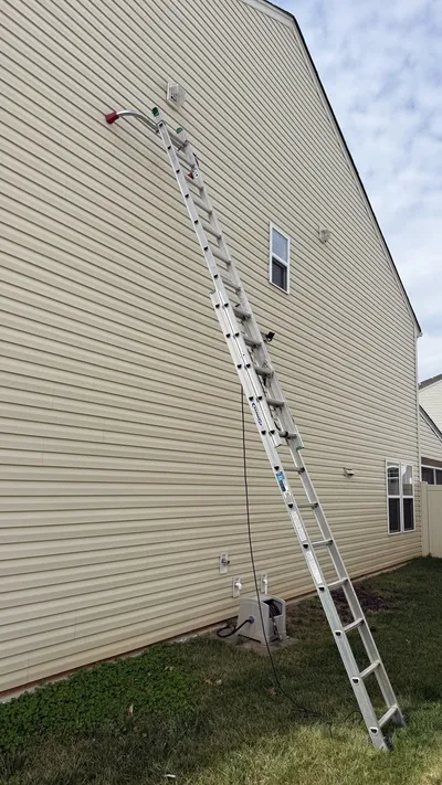 Tall ladder up to a second story dryer vent on a vinyl sided home in Reedy Fork Ranch