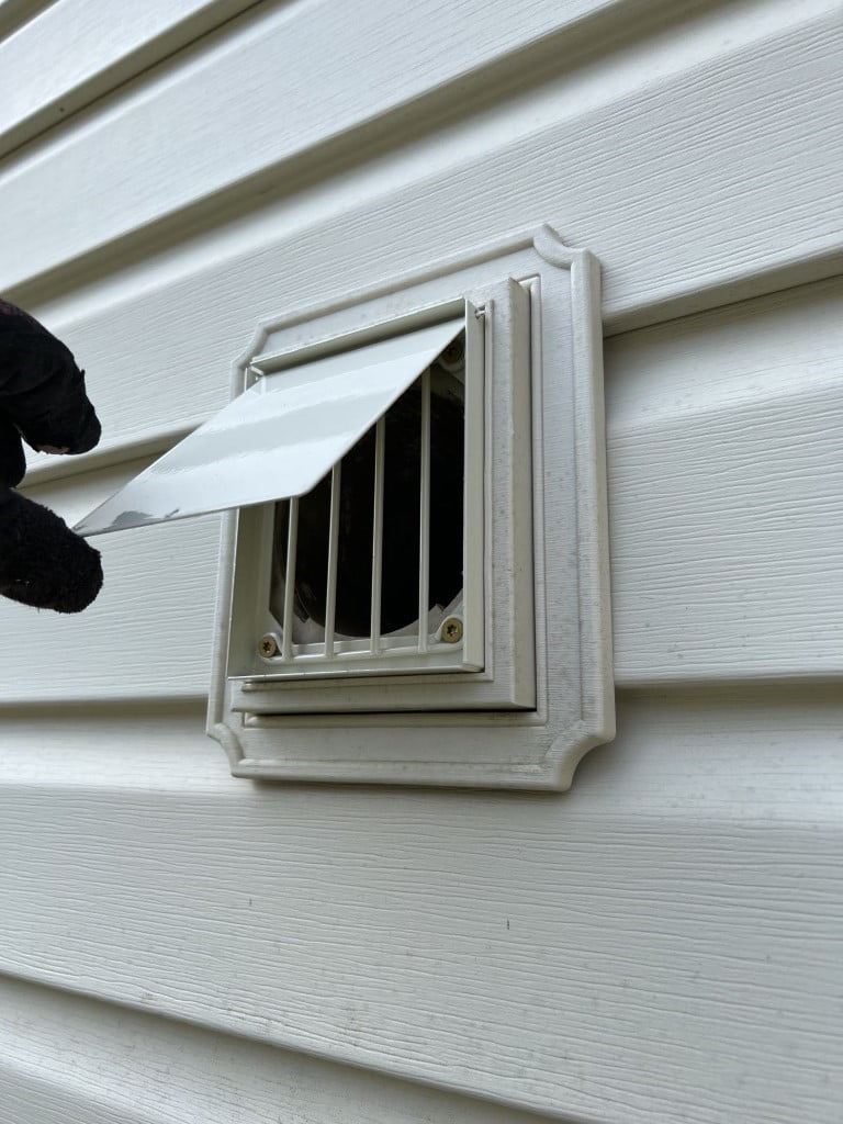 Professional lifting the flap of an exterior dryer vent.